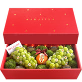 A red gift box filled with an assortment of fresh fruits, including grapes, oranges, and mandarin oranges, arranged to celebrate the Lunar New Year.